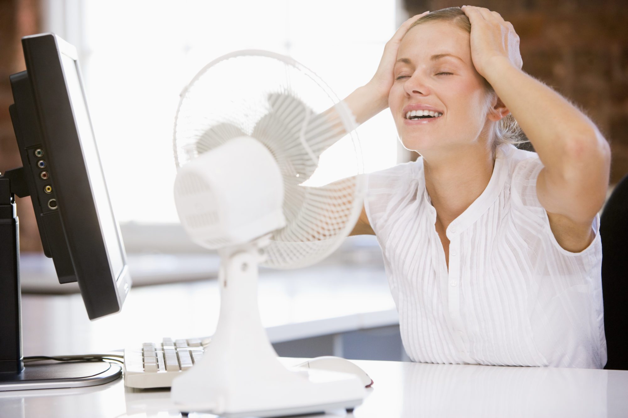 Businesswoman in office with computer and fan cooling off Businesswoman in office with computer and fan cooling off